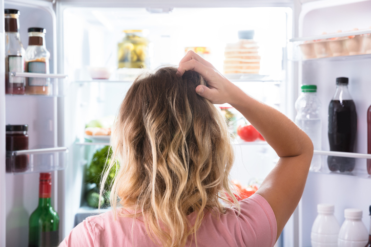Vrouw kijkt twijfelend in de koelkast 
